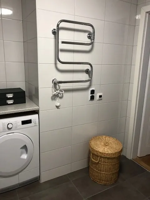 Badrum med handdukstork på väggen, tvättmaskin och tvättkorg på klinkergolv