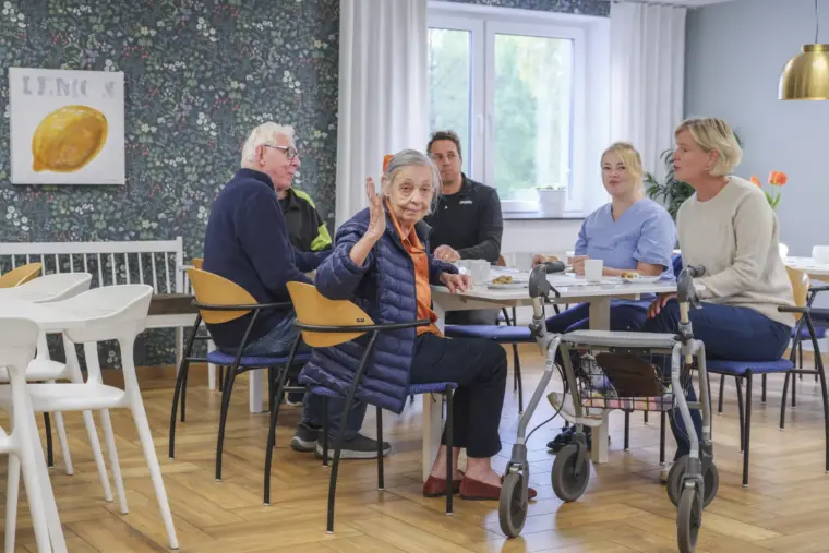 Boende fikar tillsammans i sällskapsrummet, en kvinna vinkar glatt