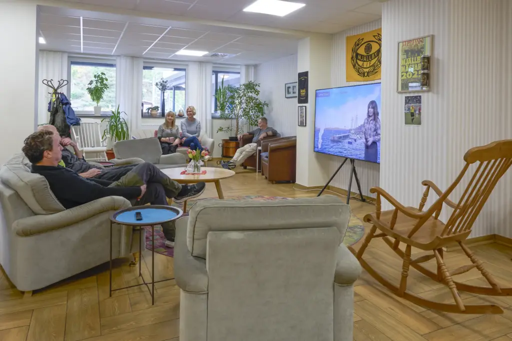 Sällskapsrum med soffor, gungstol och tv där boende umgås